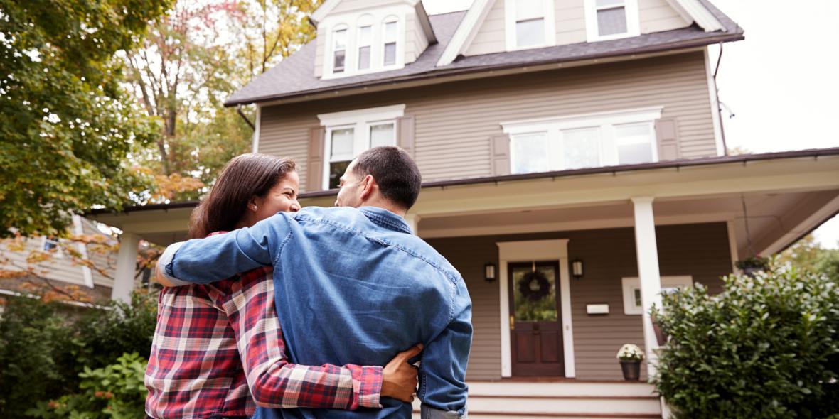 Happy couple holding each other in front of house