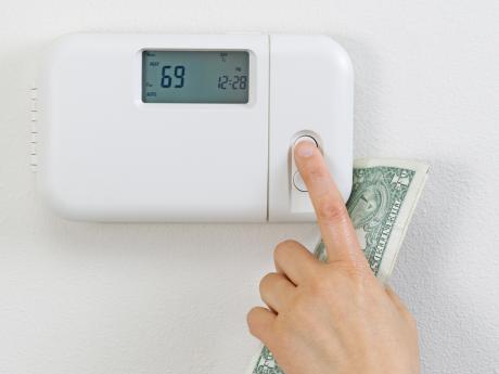 adjusting thermostat with money in hand, increasing utility bill concept