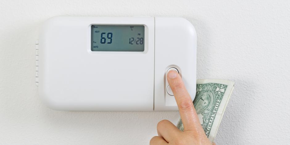 adjusting thermostat with money in hand, increasing utility bill concept